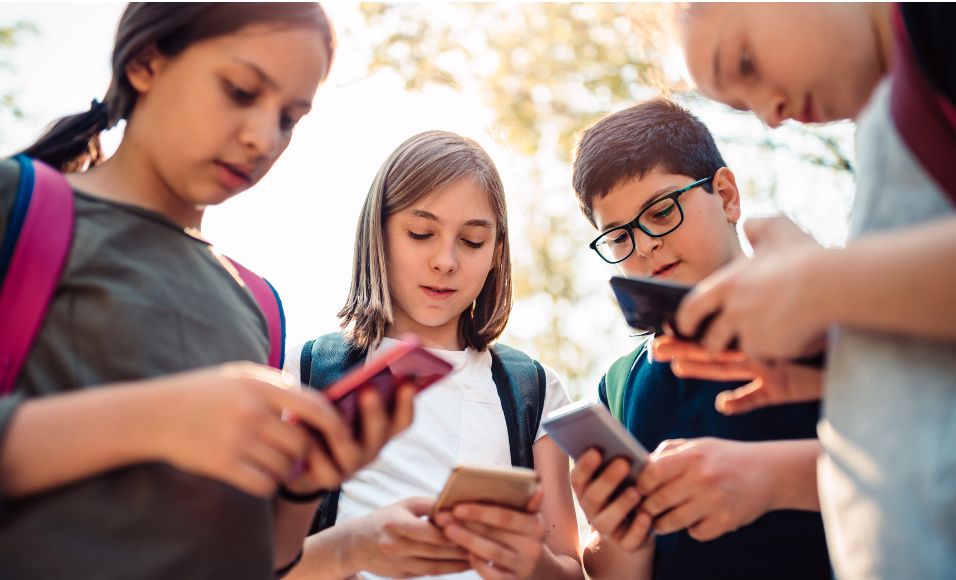 Groupe d'enfants n'ayant pas la majorité numérique utilisant tous un smartphone et probablement des réseaux sociaux.
